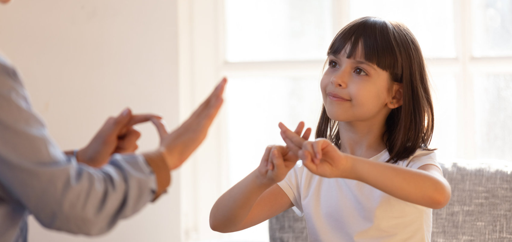 adult woman communicating with a deaf child using sign language sitting on couch in living room